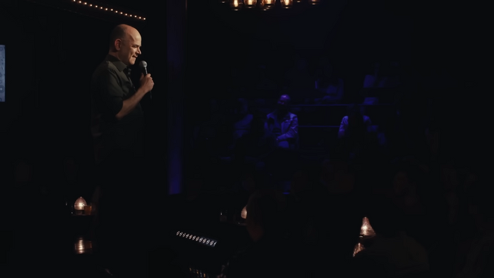 Todd Barry onstage holding a microphone.