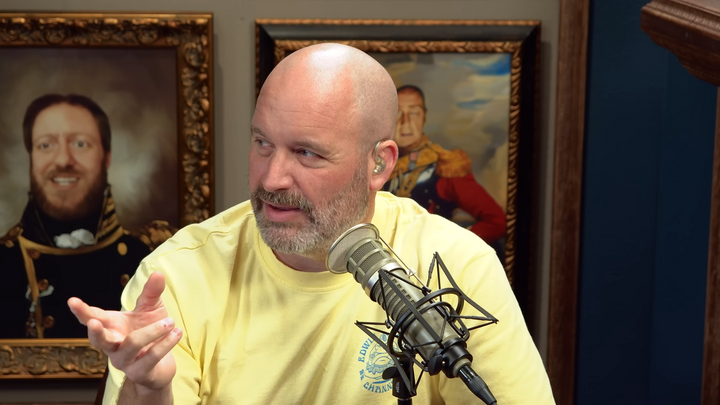 Tom Segura seated in front of a microphone in his podcast studio.